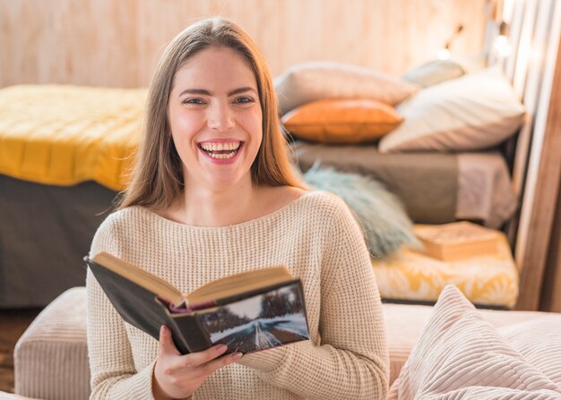 Cheerful young woman laughing while reading book at home