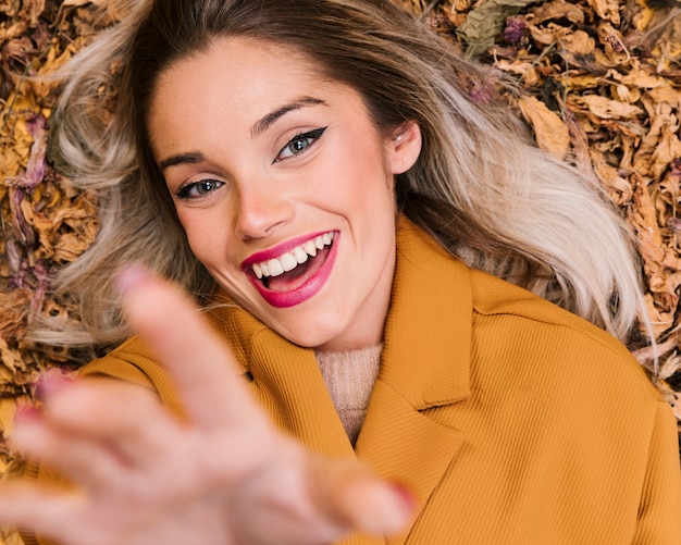 Free photo cheerful young woman lying on dry leaves at outdoors