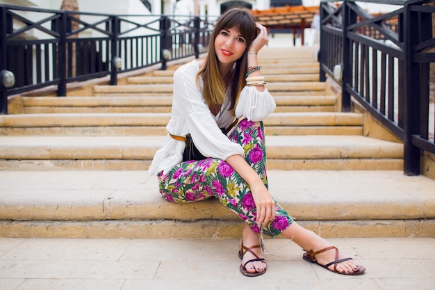 Free photo cheerful young woman  sitting on the steps, stylish summer  bright outfit, trendy hairstyle.    vacation mood. tropical print . fresh close up portrait .