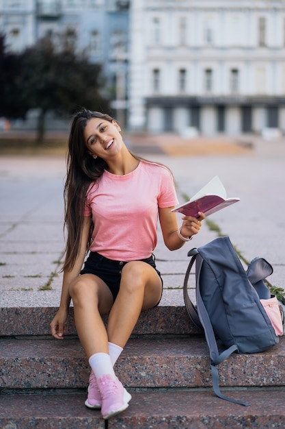 Cheerful young woman taking notes while sitting on steps on the street