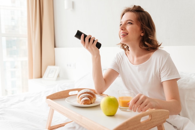 Cheerful young woman watch tv holding remote control.