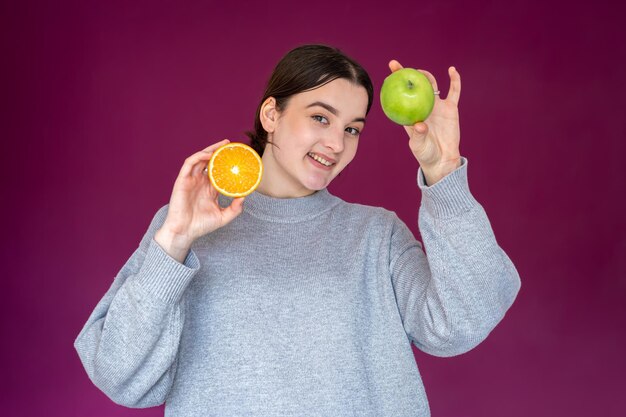 Cheerful young woman with apple and orange on purple background