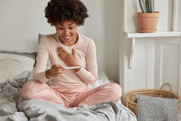 Cheerful young woman with pregnancy test posing at home