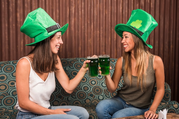 Free Photo cheerful young women clanging glasses of drink on settee in room