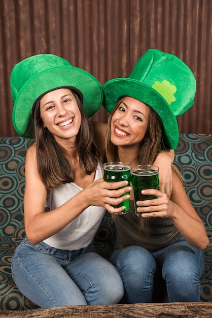 Free photo cheerful young women hugging and clanging glasses of drink on settee