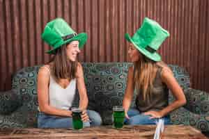 Free photo cheerful young women with glasses of drink on settee in room