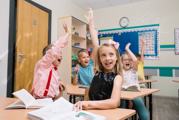 Cheering schoolkids in classroom raising hands