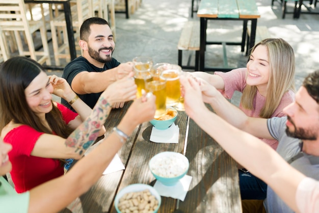 Free photo cheers! cheerful group of friends making a toast with beers. best friends enjoying some drinks together at an outdoor bar and celebrating