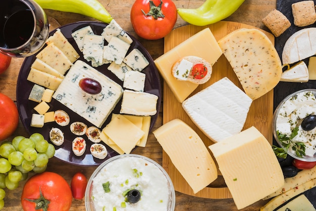 Free photo cheese blocks and slices with tomatoes, grapes and green chili pepper on table