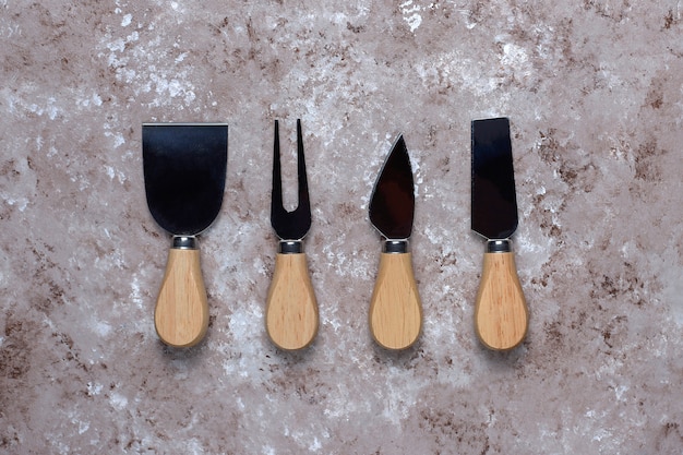 Free photo cheese knives with wooden handles, fork, spatula on light brown surface.