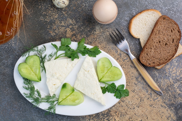 Cheese plate with vegetables and bread slices.