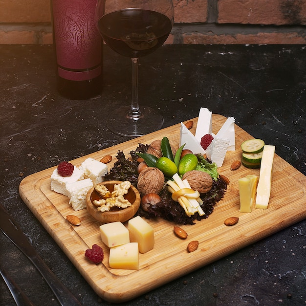 Cheese platter with different cheeses, grapes, nuts, honey, bread and dates on rustic wood. on dark wood board with wine bottle and glass of wine 