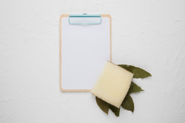 Free Photo cheese slice; dried bay leaves and clipboard on white backdrop