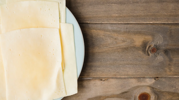 Free photo cheese slices on white plate against wooden plank backdrop