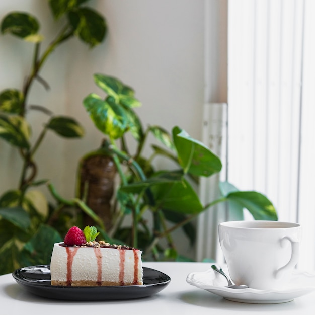 Cheesecake with berries; coffee cup on table in cafe near the plant