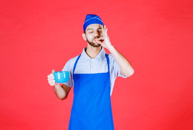 Chef in blue apron holding a blue ceramic cup and enjoying the taste of the product. 