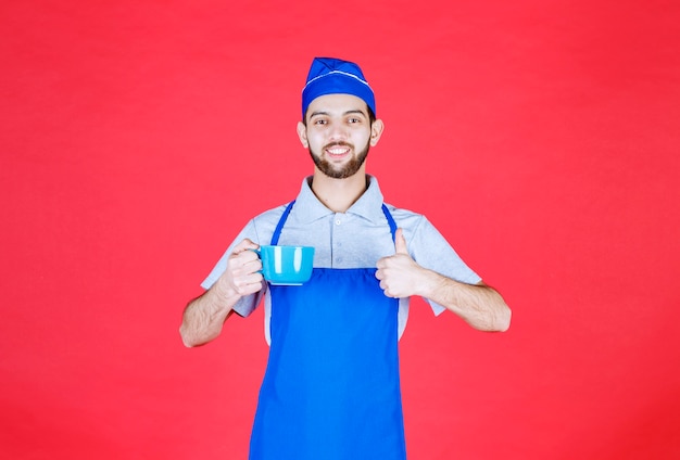 Chef in blue apron holding a blue ceramic cup and enjoying the taste of the product. 