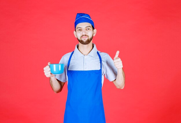 Chef in blue apron holding a blue ceramic cup and enjoying the taste of the product. 