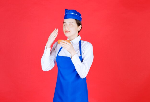 Chef in blue apron holding a pottery bowl and smelling the flavour. 