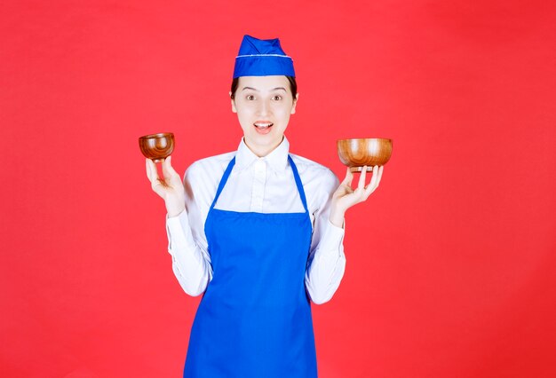 Chef in blue apron holding two pottery chinese tea cups at her both hands. 