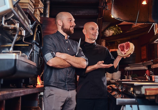 Chef and his assistant presenting a fresh steak before cooking in a restaurant kitchen.