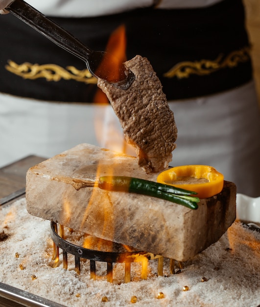 Free photo chef holding beef steak on stone with grilled peppers on fire