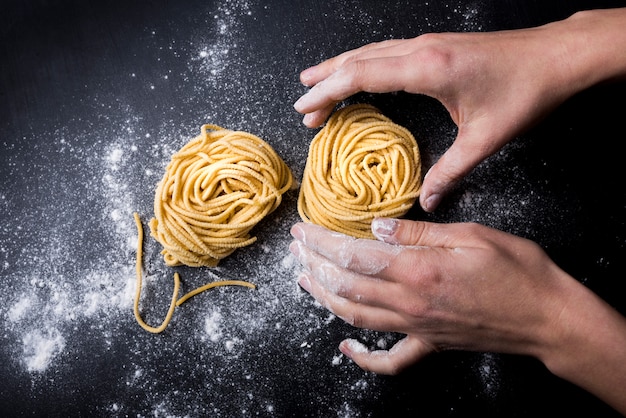 Chef making tagliatelle pasta nest with powder flour on kitchen table