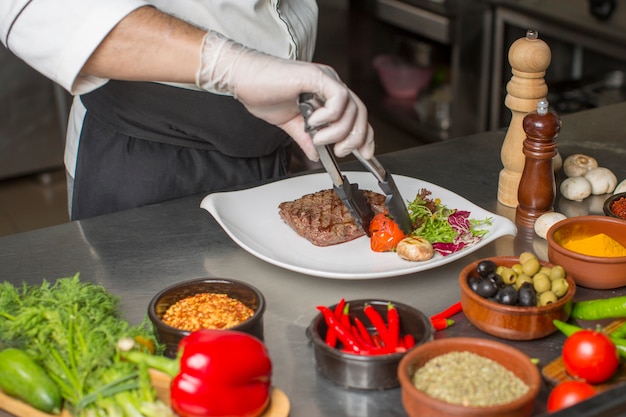 Free Photo chef preparing beef steak for service with salad and grilled vegetable