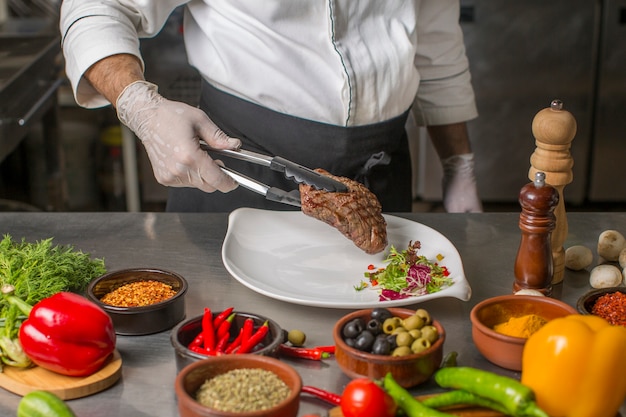 Free photo chef putting grilled steak to the serving plate with herbs salad