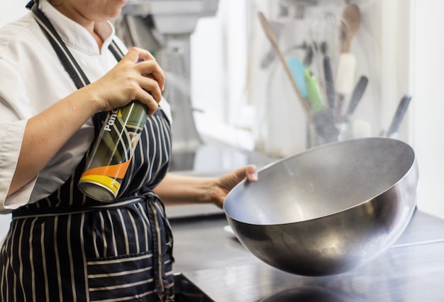 Chef spraying oil on a lard round bowl with a blurred background