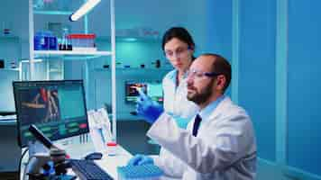 Free photo chemist doctor explaining to nurse vaccine development in modern equipped laboratory holding test tube with blood sample