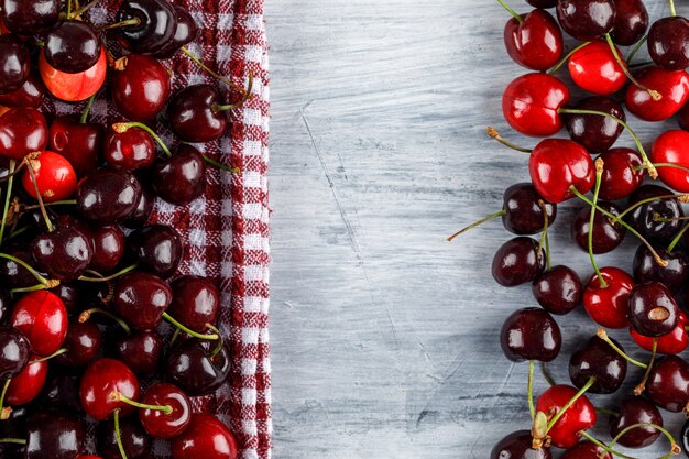 Cherries on grunge and picnic cloth surface, flat lay.