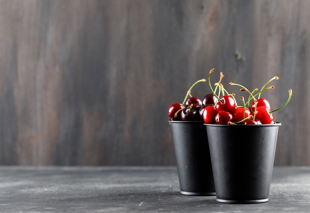 Free photo cherries in mini buckets side view on grunge and grey surface