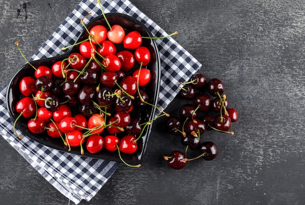 Free photo cherries in a plate flat lay on picnic cloth and grey surface