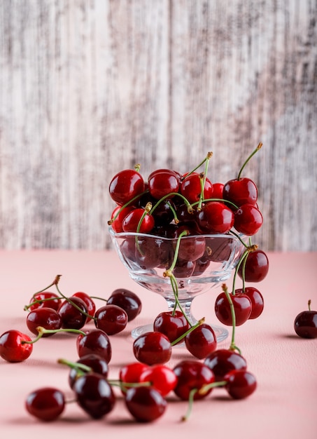 Free photo cherries in a vase on pink and grungy surface