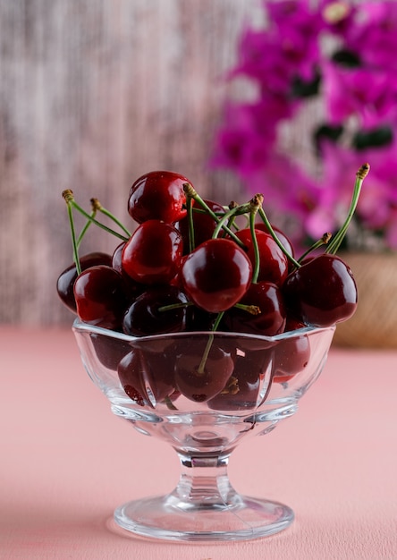 Free photo cherries with flower pot in a vase on pink and grungy surface, close-up