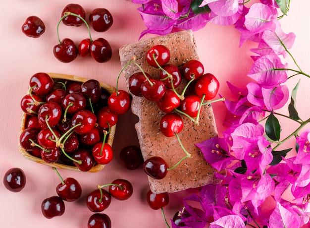 Free photo cherries with flowers, brick in a wooden plate on pink surface