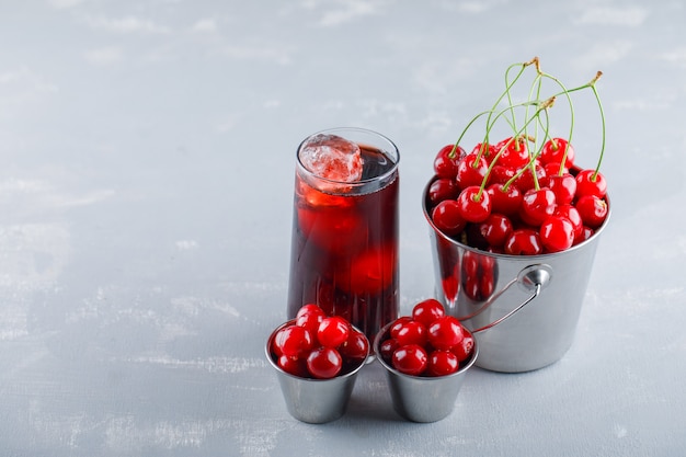 Free photo cherries with juice in buckets on plaster space, high angle view.