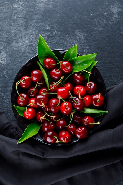 Free Photo cherries with leaves in a plate on grey plaster and textile surface