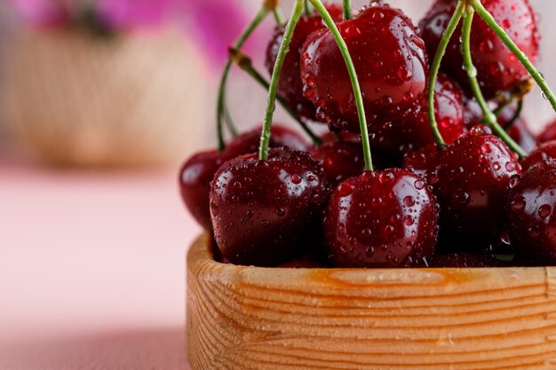 Cherries in a wooden plate with flower pot close-up on a pink surface