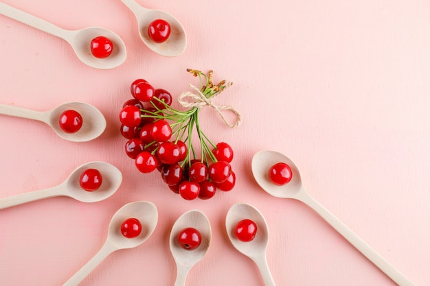 Cherries in wooden spoons on pink space, flat lay.