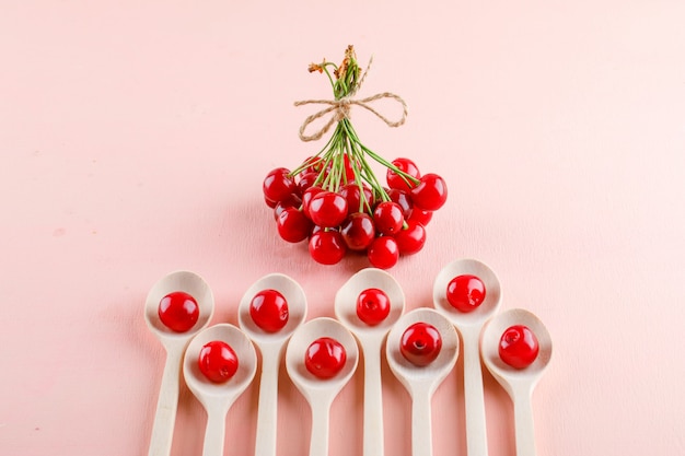 Free Photo cherries in wooden spoons on a pink table. flat lay.