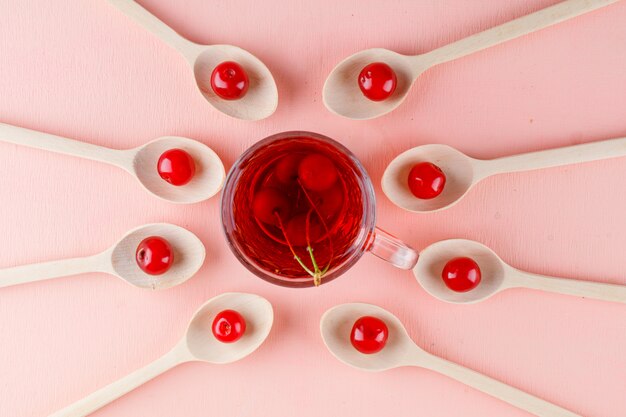 Cherries in wooden spoons with tea flat lay on a pink space