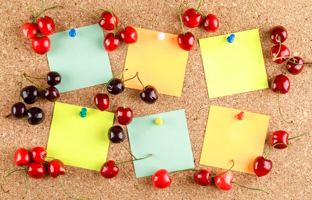 Cherry berries with pinned notes on light surface, flat lay.