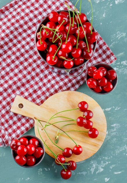 Cherry in buckets with cutting board flat lay on plaster and kitchen towel