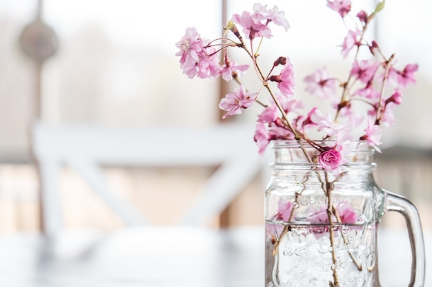 Cherry flowers and branches in a glass of water on the table under the lights