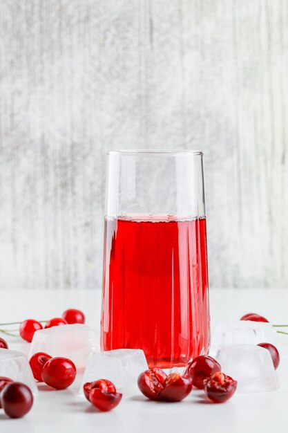 Cherry juice with cherries, ice cubes in a glass on white