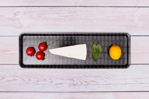 Free photo cherry tomato; cheese; bay leaves and lemon on black tray over wooden surface