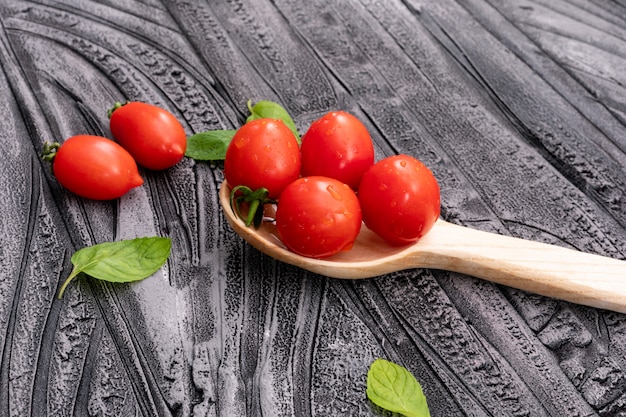 cherry tomato in wooden spoon other tomatoes and leaves on wooden texture