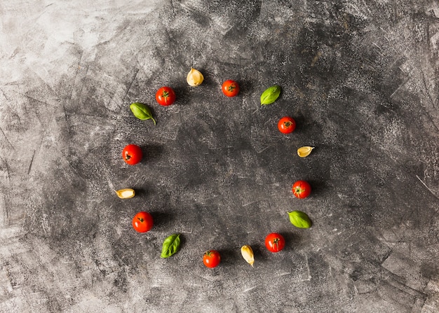 Free Photo cherry tomatoes; basil and garlic cloves arranged in circular frame on grunge background